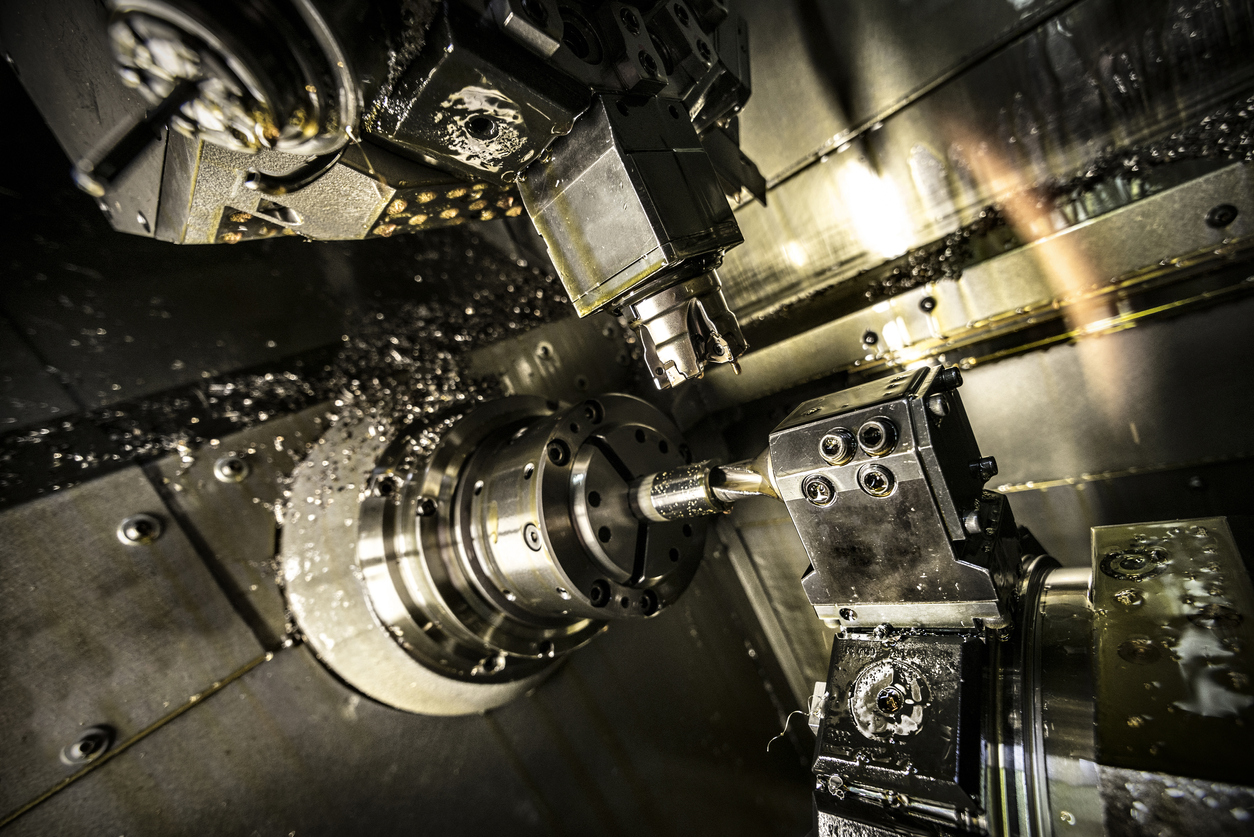Interior of CNC lathe with rotating chuck, cutting tool turret, and metal workpiece amid coolant and chips
