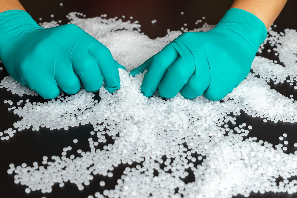 Gloved hands sorting white plastic polymer pellets scattered on a black surface
