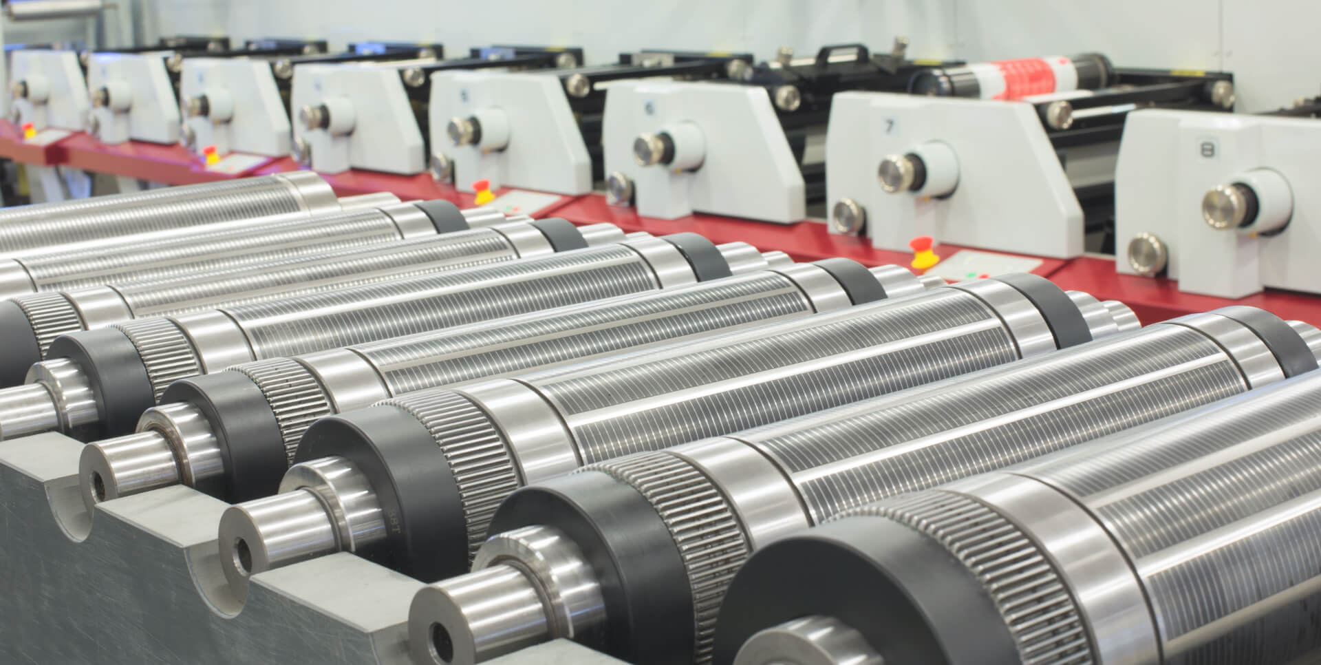 Rows of polished metal spindles with knurled shafts on a machine bed in an industrial workshop