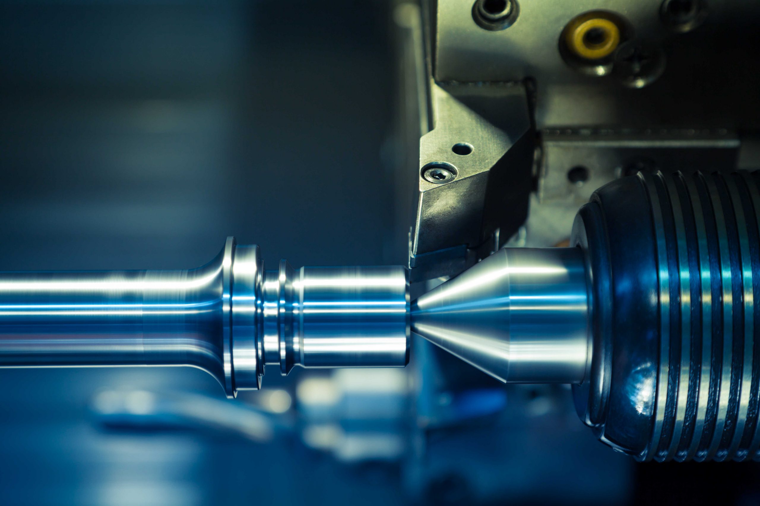 Close-up of CNC lathe spindle machining a shiny metal shaft with cutting tool and chuck in blue-lit workshop
