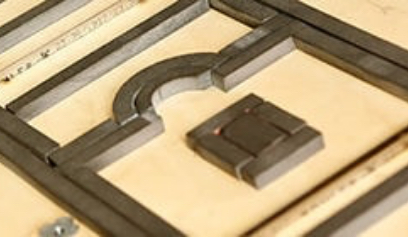 Close-up of a die-cutting board with wooden frame and curved metal cutting rule around a small rectangular cutout