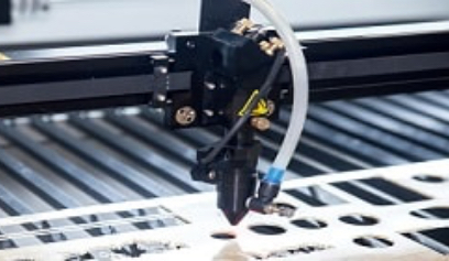 Laser cutting head with air hose moving over a metal sheet, cutting circular and slotted patterns on a CNC bed