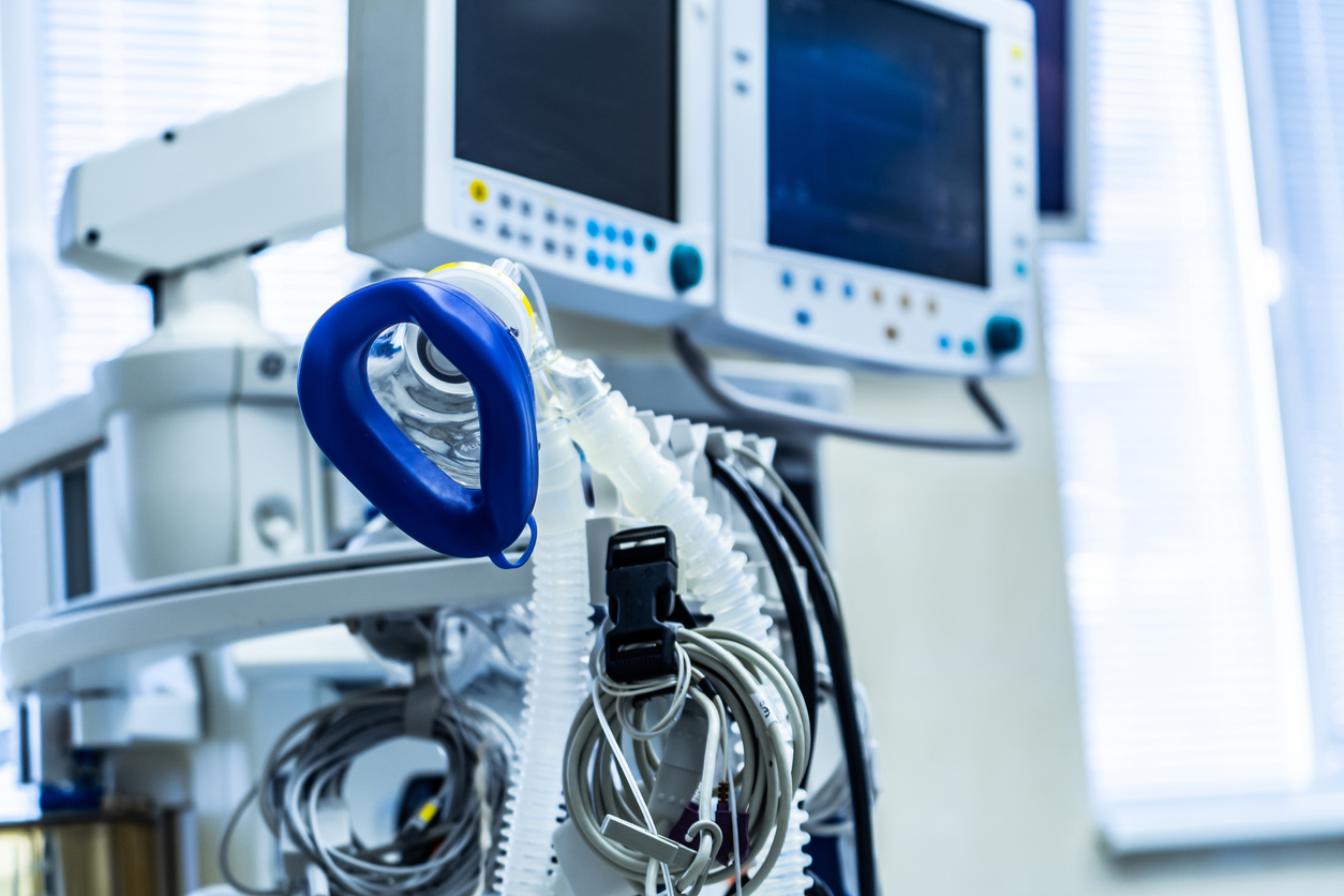 Ambu bag and breathing tubes on a hospital ventilator cart with patient monitors in the background