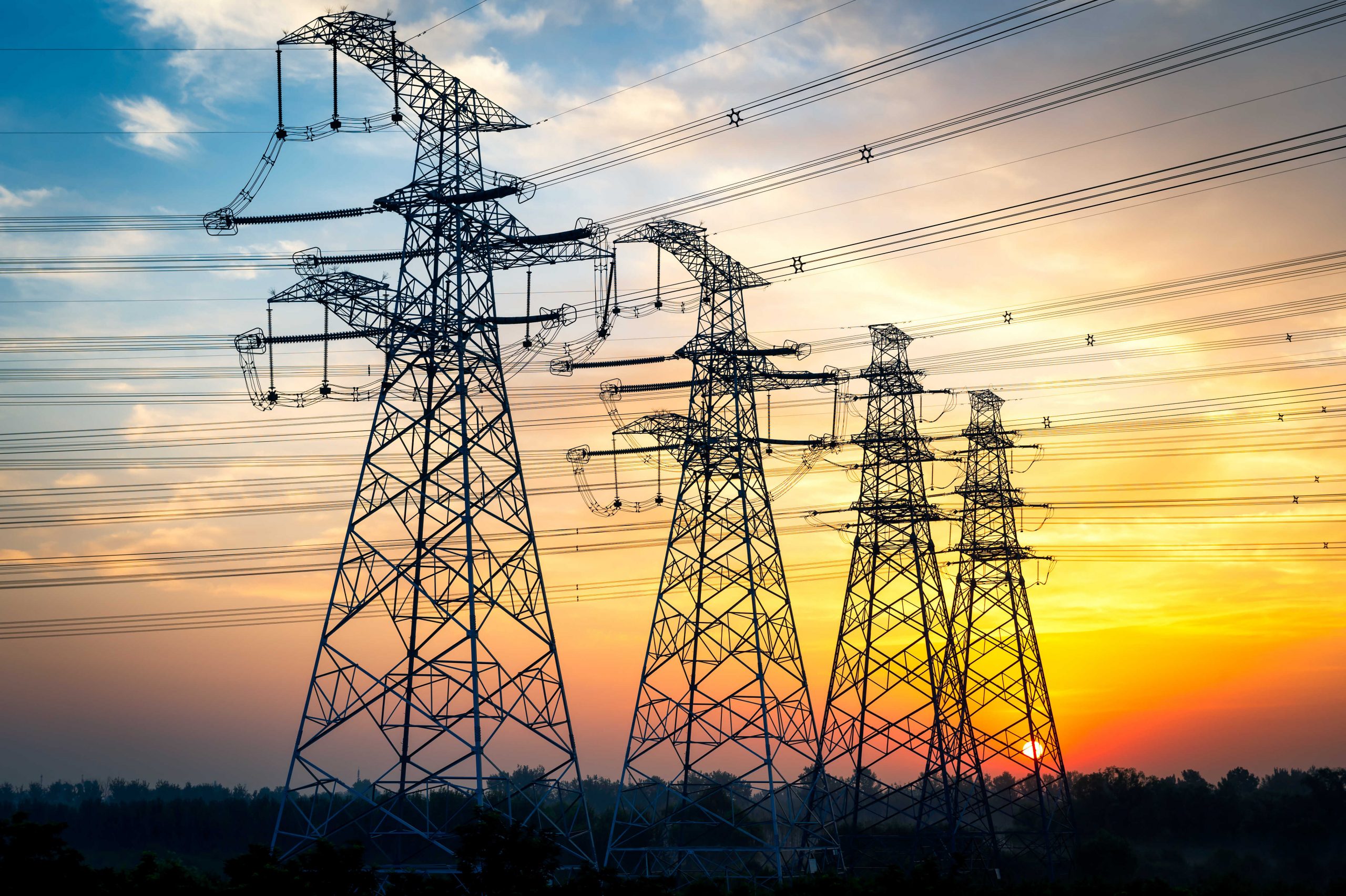 High-voltage transmission towers and power lines silhouetted against a colorful sunset sky