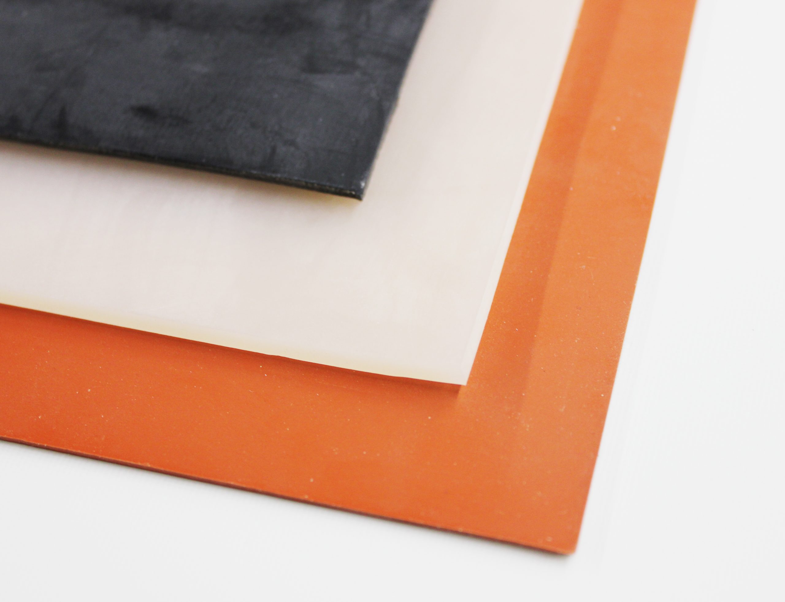 Stacked rubber sheets in black, white, and orange on a white background, showing corner close-up