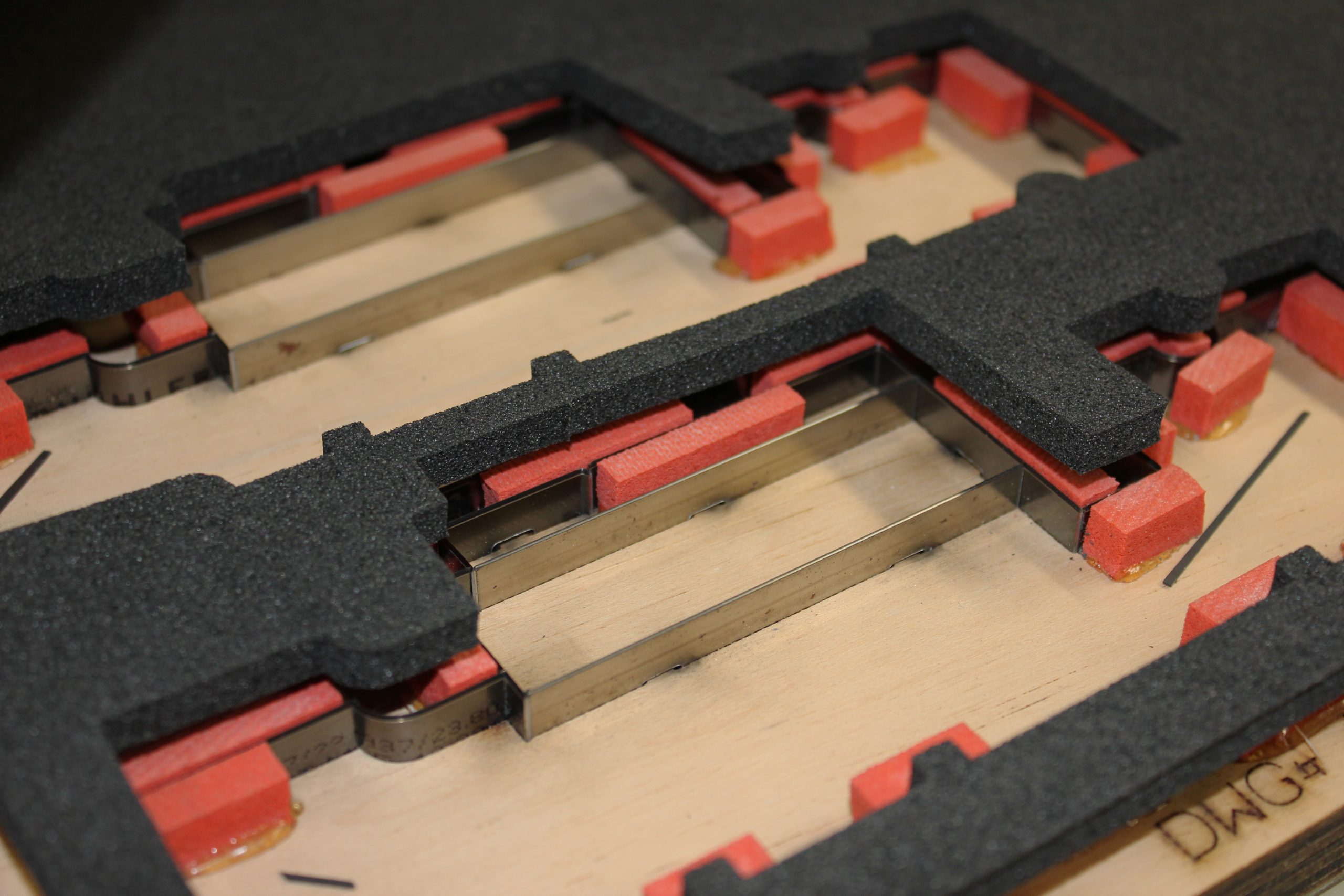 Close-up of EVA foam die-cutting mold with metal cutting blades and red spacers mounted on a wooden base