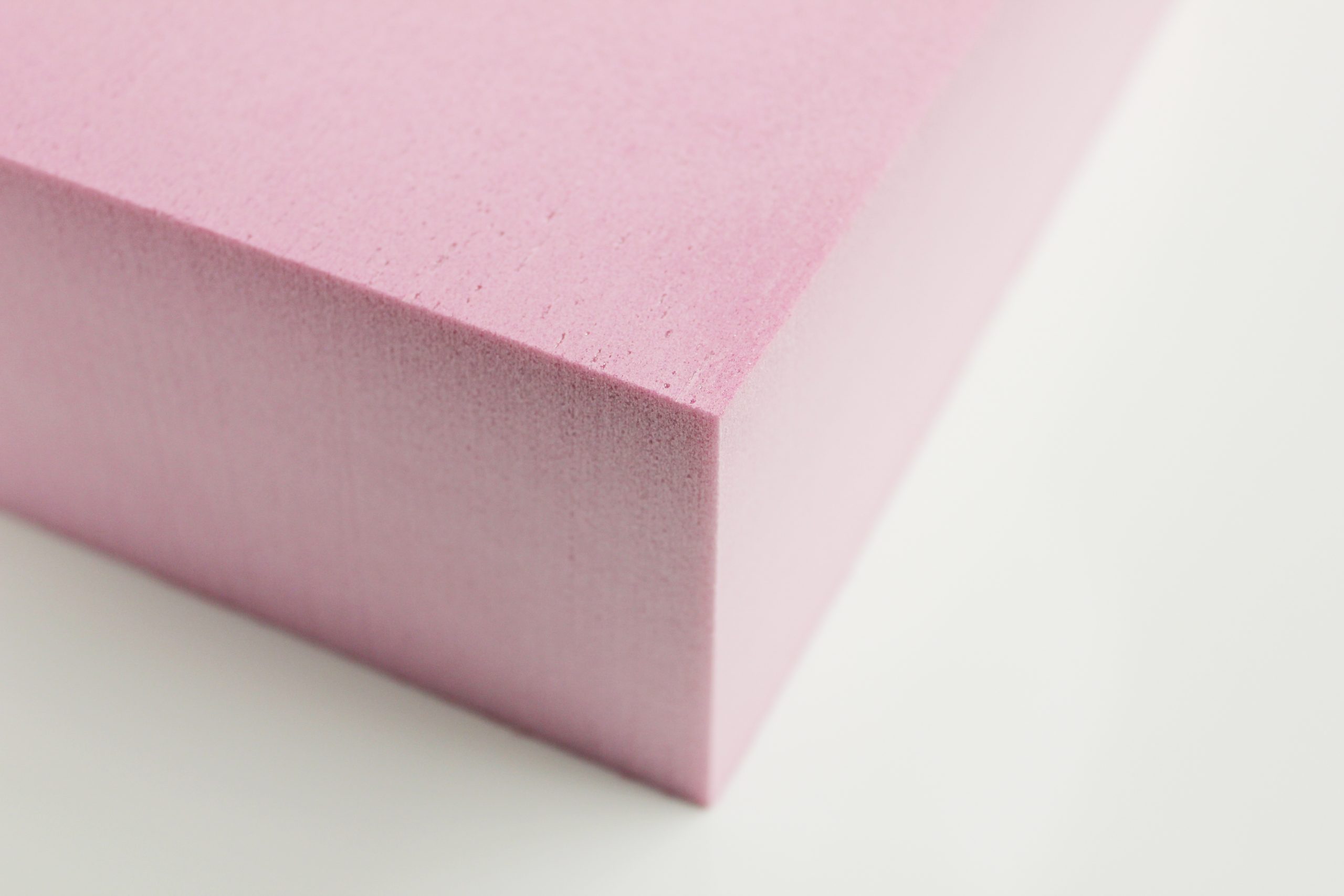 Close-up of pink rigid foam insulation board corner with smooth surface texture on a white background