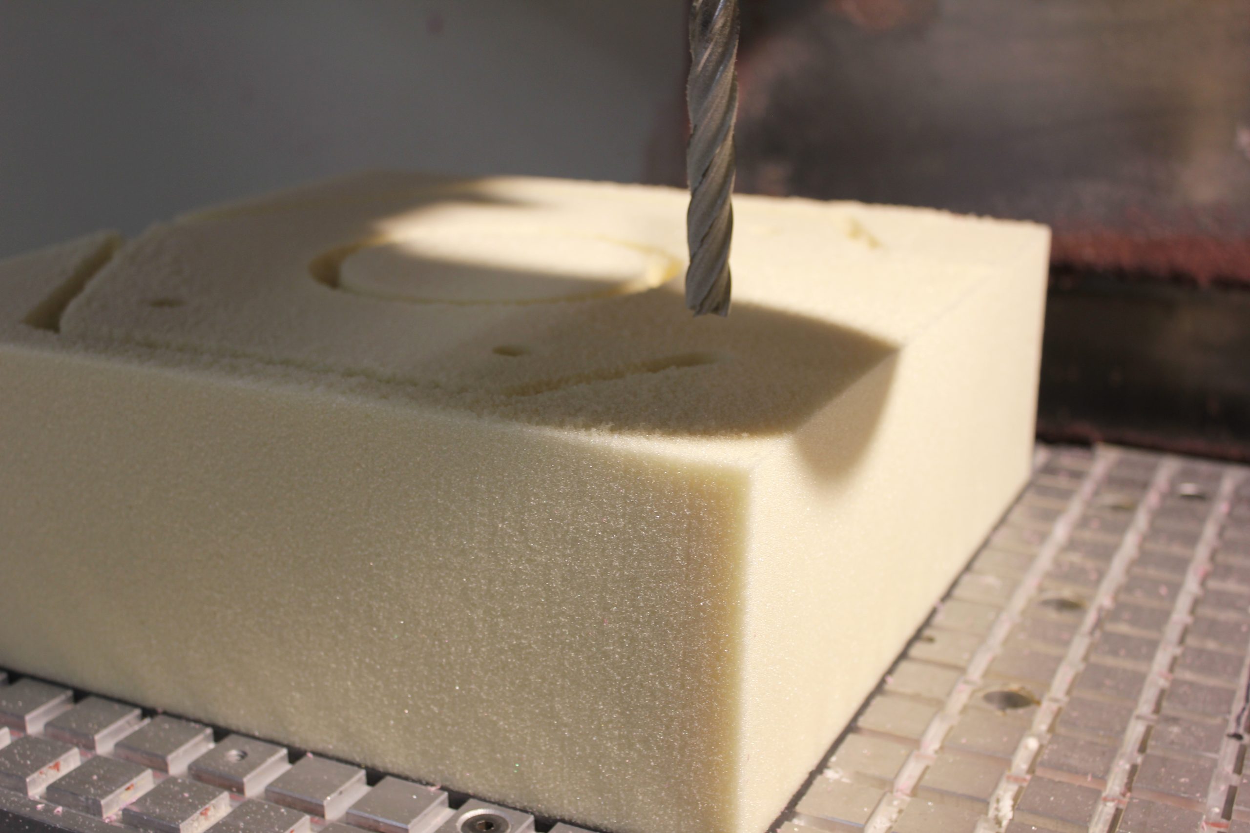 CNC end mill carving a recessed circular pocket into a foam block on a machine bed in a workshop setting