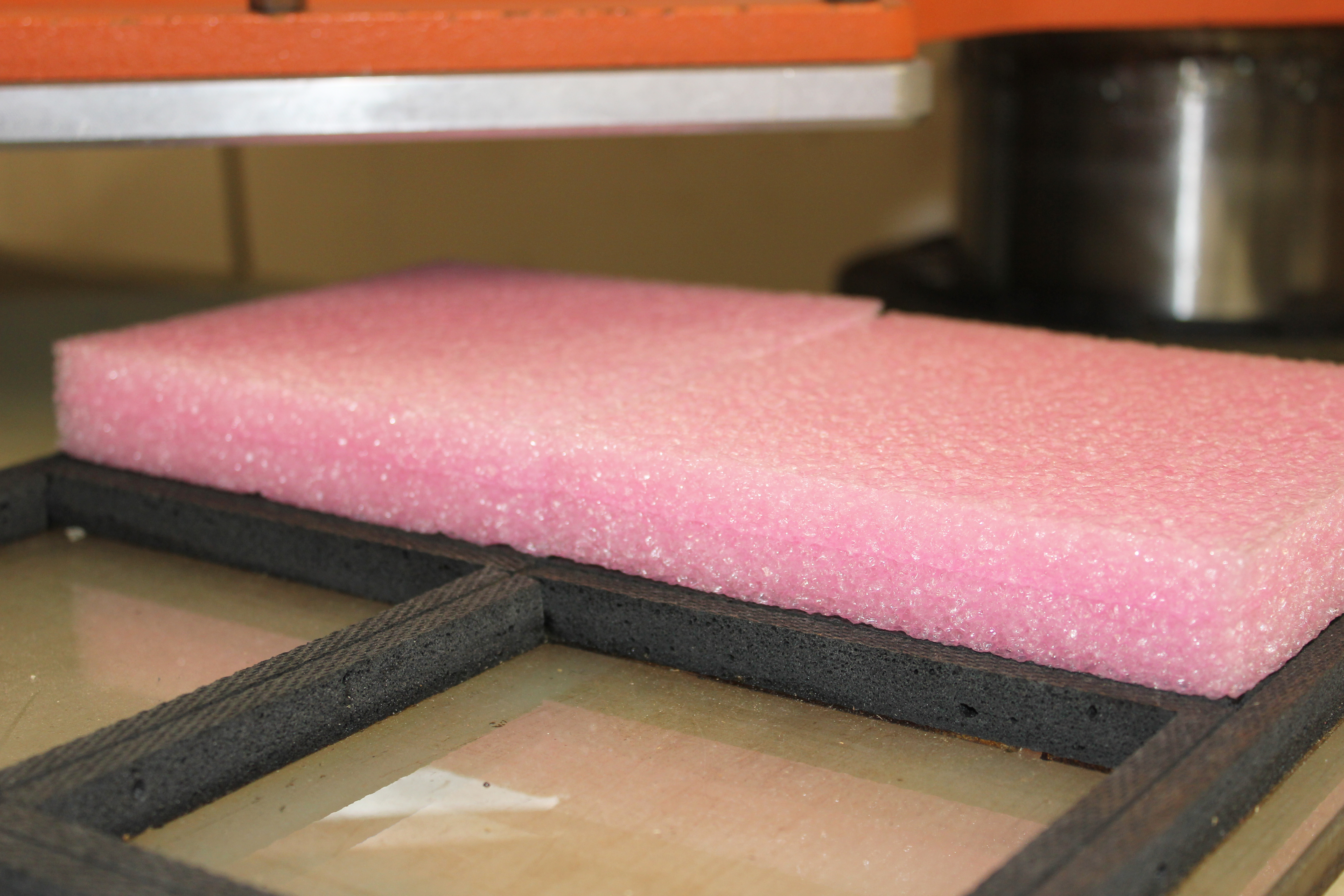 Pink packaging foam sheet on a die-cutting press with black foam frame on the cutting table