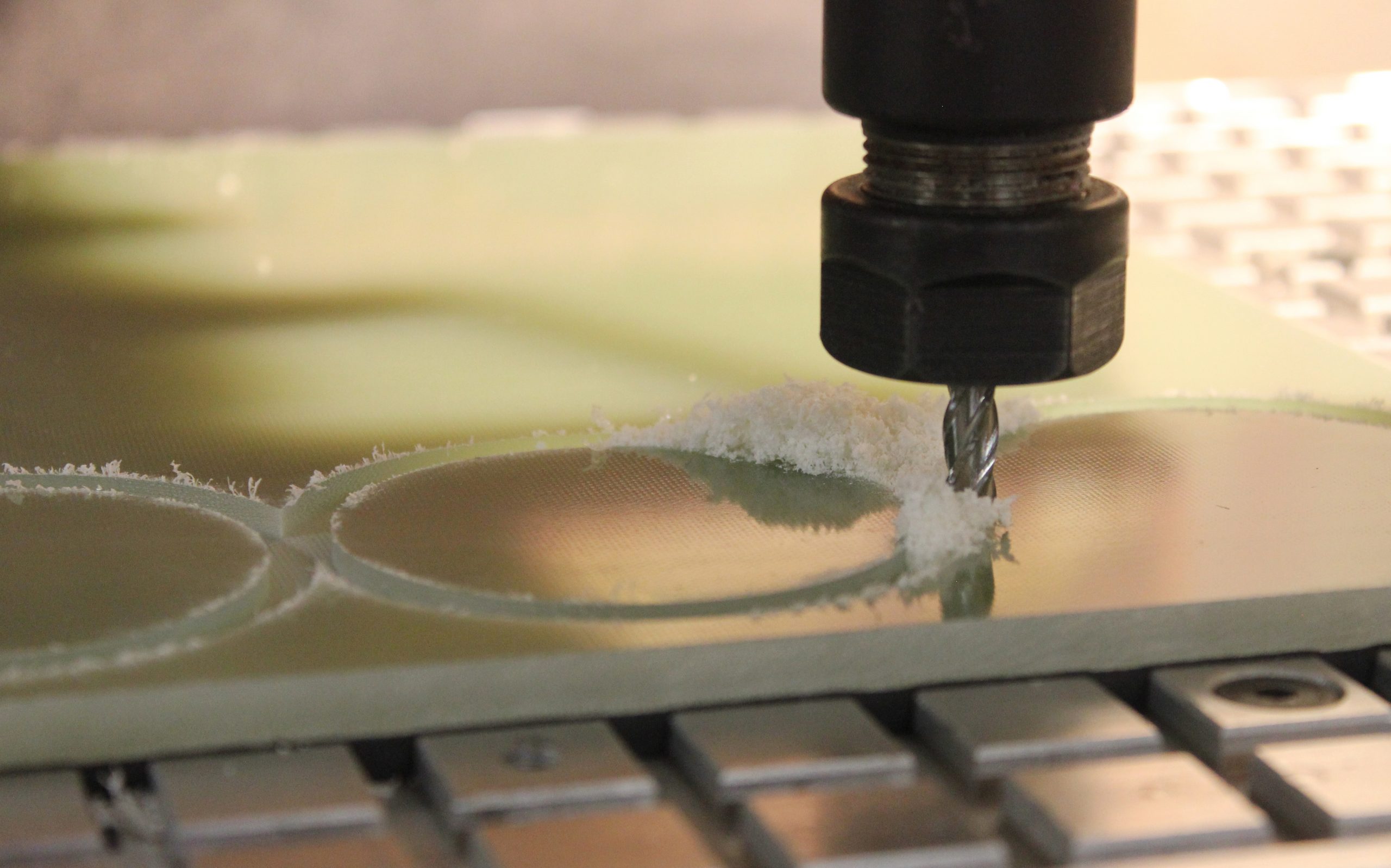 CNC end mill cutting circular pockets in a green phenolic sheet, with white machining dust around the toolpath
