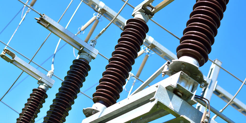 High-voltage substation with brown ceramic insulators and metal busbars against a clear blue sky