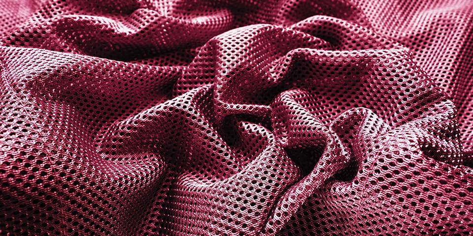 Close-up of burgundy perforated rubber or neoprene fabric with textured holes and folds