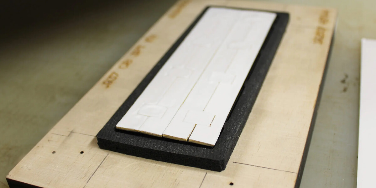 Die-cut white gap pad pieces on black foam sheet placed on a wooden cutting board