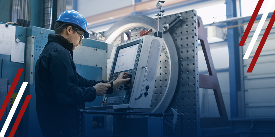 Operator in hard hat adjusting controls on a CNC machine control panel in an industrial workshop