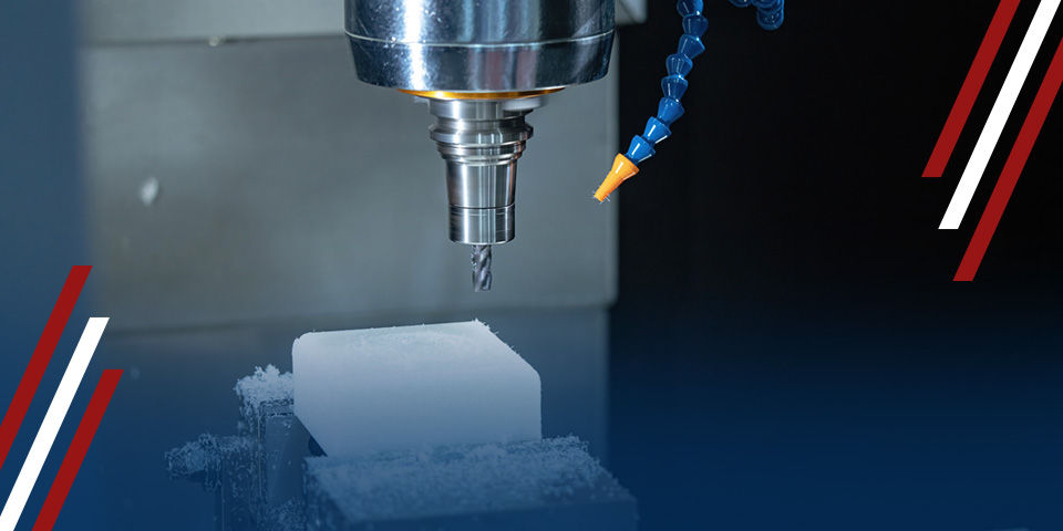 CNC milling machine spindle and cutting tool above a white plastic block, with blue coolant hose in industrial workspace