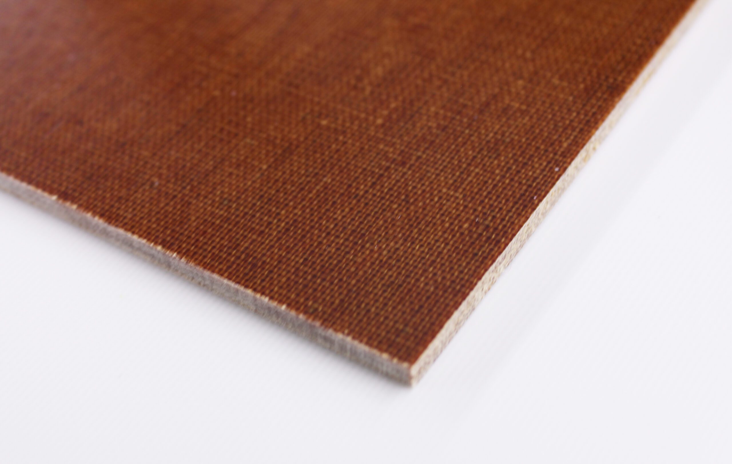 Close-up of brown phenolic laminate sheet edge showing textured surface and layered core on a white background