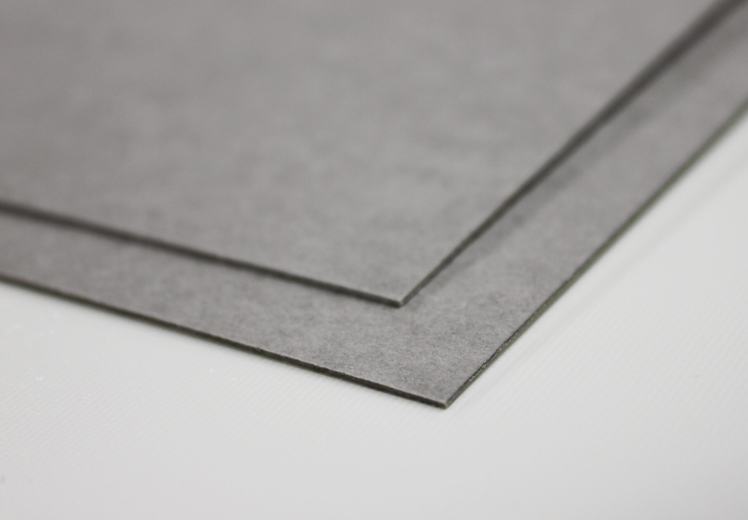 Stacked gray sheet material with sharp edges on a white surface, close-up of layered panels