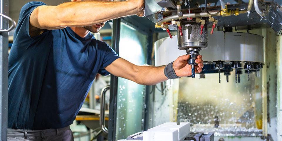 Operator adjusting CNC milling machine spindle and tool above workpiece with coolant spray in a manufacturing workshop