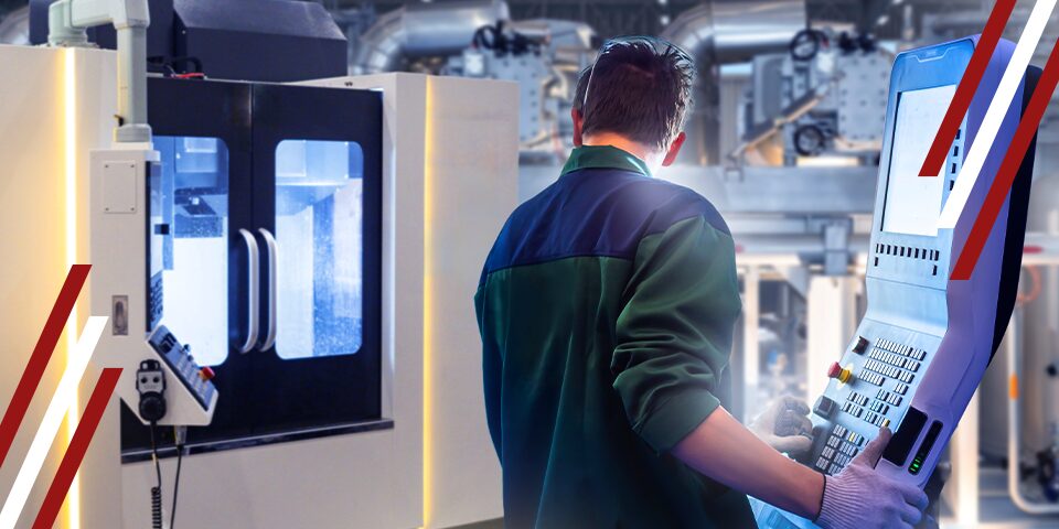 CNC machinist operating a control panel beside a milling machine in a modern factory workshop